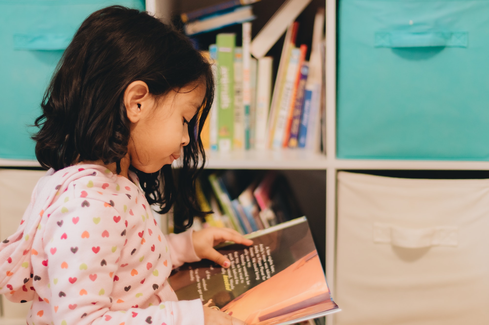 Diverse pre school girl at home in bed room happily reading from books